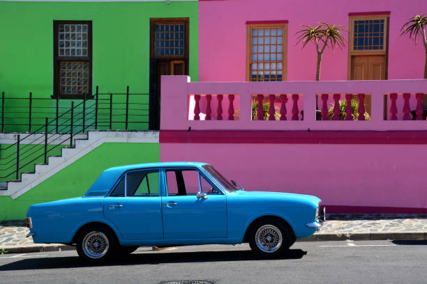 an old but beautiful blue car in front of colourful houses in the quarter of Bo kaap the muslim quarter in Capetown South Africa . It was in February